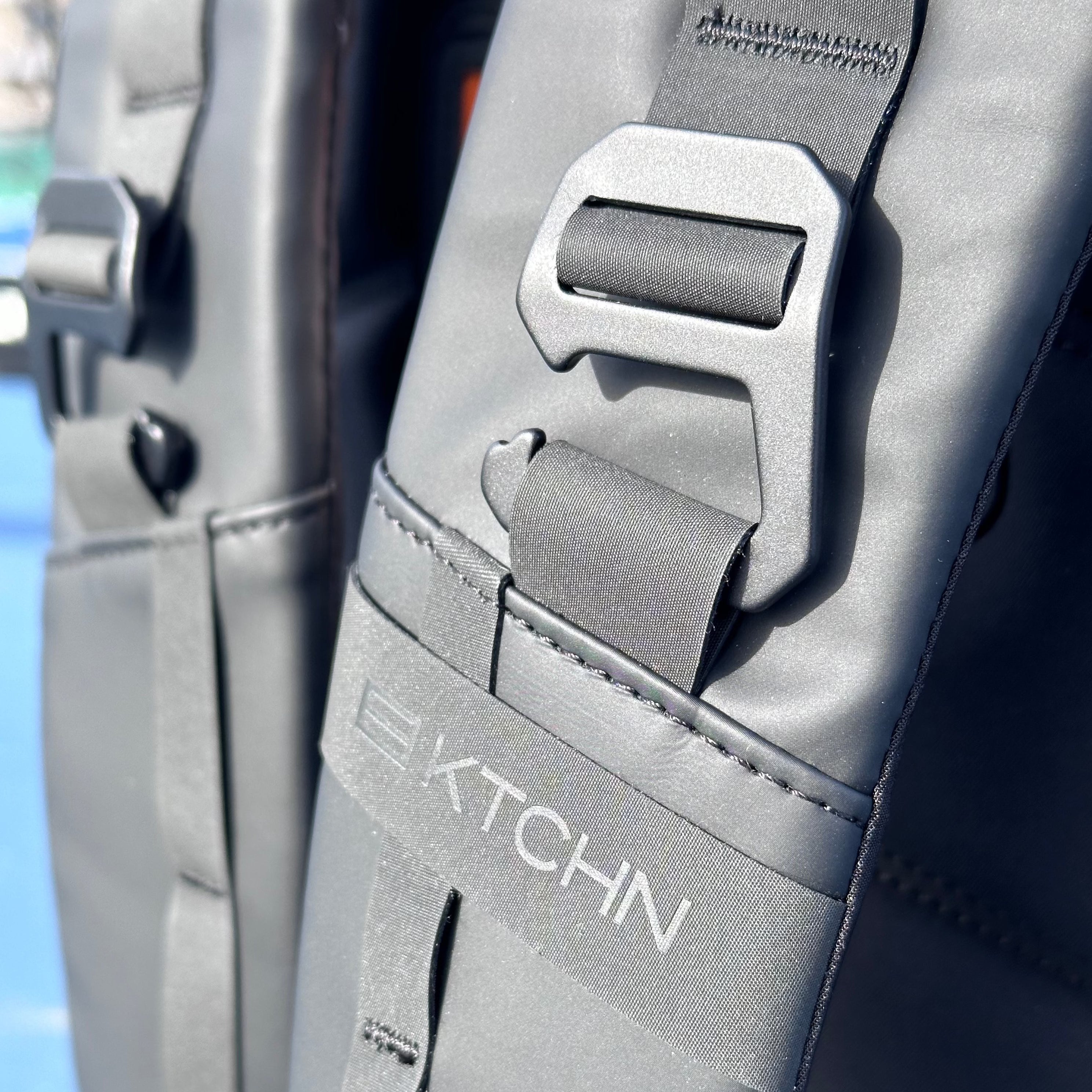 Close-up of a black bag with a buckle and the word 'KTCHN' on a strap.